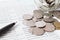 Coins scattered from glass jar, pen and savings account passbook or financial statement on office desk table