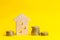 Coins and wooden house on a yellow background. Concept of real estate. Buying, selling and renting a house. Loan for an apartment,