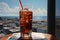 Cola drink with ice in glass on wooden table in cafe, sea and town on background