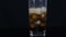 Cola is poured into a large long glass cup with pieces of ice inside on a black background.