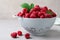 Colander with delicious ripe raspberries on table against light background