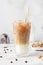 Cold coffee with milk and ice cubes in a tall glass with bamboo straw, light grey background.