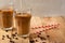 Cold coffee pouring in cream, milk in transparent glasses with ice and straws, on a wooden background, a cooling drink, refreshing