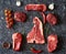 Cold cuts - raw, aged, juicy steaks of filet mignon, t-bone, ribeye, striploin, on a dark stone background with rosemary sprigs