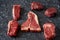 Cold cuts - raw, aged, juicy steaks of filet mignon, t-bone, ribeye, striploin, on a dark stone background. Top view, assortment