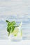 Cold detox summer mineral water with lime, mint, ice, straw on soft blue wood background, copy space.