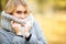 Cold and flu. Young woman in a gray coat walking in the autumn park and warms frozen hand