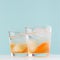 Cold fruit beverage with oranges liquor and mineral water, ice in misted glass in modern elegant pastel blue interior, square.