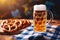 Cold full beer mug with Beirian pretzels on the wooden table covered with traditional blue and white tablecloth during Oktoberfest