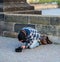 Cold Homeless man on his knees begging for money from tourists on the Charles Bridge in Prague - Spring 2019