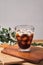 Cold iced black brew coffee in a glass with pieces of ice on a wooden table, natural light, fresh summer drink