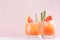 Cold lemonade of fresh grapefruit juice, alcohol and ice cubes decorated slice citrus and twig rosemary on fashion pastel pink.