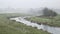 Cold misty Winter landscape over stream in English countryside