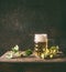 Cold mug of beer with foam on a rustic table with a vine and cones of hops opposite a dark wall