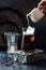 Cold refreshing iced coffee in a tall glass and coffee beans on dark background. Pouring cream into glass with iced coffee.