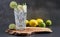 Cold refreshing limonade, mojito or gin tonic in glass, with fresh mint and ice cubes, lime and lemon on wooden board and black