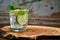 Cold refreshing summer limonade, mojito or gin tonic in glass, with fresh mint and ice cubes, lime and lemon on wooden board.