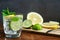 Cold refreshing summer limonade, mojito or gin tonic in glass, with fresh mint and ice cubes, lime and lemon on wooden table, on