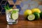 Cold refreshing summer limonade, mojito or gin tonic in glass, with fresh mint and ice cubes, lime and lemon on wooden table, on