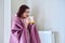 Cold season, woman with plaid mug of hot tea warming near wall heating radiator