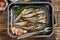 Cold Smoked sprat fishes in a kitchen tray with spices. Wooden background. Top view