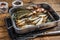 Cold Smoked sprat fishes in a kitchen tray with spices. Wooden background. Top view