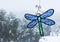 Cold snow day with oak trees seen through a window with bright blue and green stained-glass dragonfly sun catcher hanging in windo