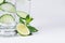 Cold spring drink with cucumber, pieces of lime, fresh leaves mint and ice on soft white background, closeup.