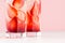 Cold strawberry juice in misted glass with sliced berries, ice cubes on white wooden table and pink, closeup, bottom section.