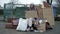 Cold, unkempt-looking young woman sits with a begging cup by a pile of rubbish and holds up a handwritten CRISIS poster.