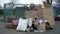 Cold, unkempt-looking young woman sits by a pile of rubbish and holds up a handwritten SELL BITCOIN poster. Woman is