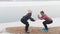 Cold weather. Two slim women in jackets doing squats on the snowy beach