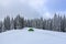 Cold winter day. Green tent stands on the snowy lawn. High spruce trees. Touristic camping rest place. Mountain landscape.