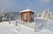 Cold winter day. On the lawn there is wooden church covered with snow high on the mountains and around it there is a forest with