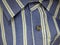 Collar and button on a mans shirt. Gva blue thread, brown button. Striped gray-blue fabric on casual wear. Assortment of men`s