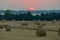 Collected and dried hay in a large meadow. Against the background of trees and the setting sun for their tops.