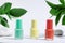 Collection of colored nail polishes, for manicure or pedicure, on a white background with hard shadows and green leaves. Creative