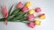 A collection of delicate paper tulips in shades of pink and yellow, artfully arranged with their green stems splayed across a