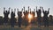 College graduates in robes waving at sunset.