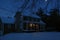 Colonial house at night with snow covered ground and moon shinning above tree limbs
