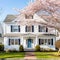 Colonial style white wooden cladding family house exterior. Beautiful front yard landscaping design with lawn and flower bed.