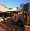 Colonnade of Sydney Opera House Australia with wood tables, seats and umbrellas for outdoor dining, and cityscape of downtown