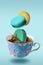 Color French macaroons falling in to the decorated blue porcelain teacup