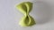 Colored bow tie pasta. Closeup single green farfalle on gray background.