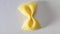 Colored bow tie pasta. Closeup single orange farfalle on gray background.