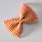 Colored bow tie pasta. Closeup single orange farfalle on gray background