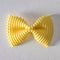 Colored bow tie pasta. Closeup single yelow farfalle on gray background