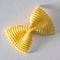 Colored bow tie pasta. Closeup single yelow farfalle on white background