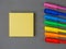 Colored bright rainbow pens and yellow square sticky post it paper sheets laying on grey background