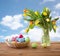 Colored easter eggs in basket and flowers over sky
